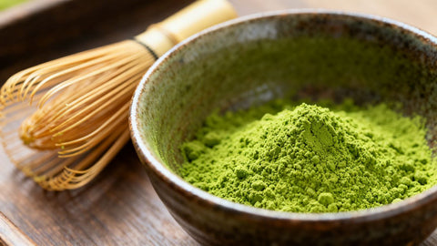 Premium matcha powder and bamboo whisk in a ceramic bowl.
