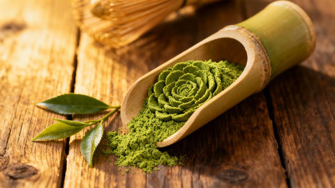 Vibrant green matcha powder and tea leaves on a wooden surface.