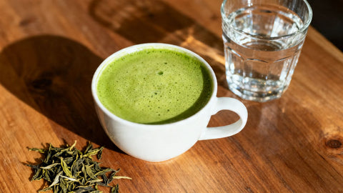 Matcha latte and glass of water on a wooden surface.